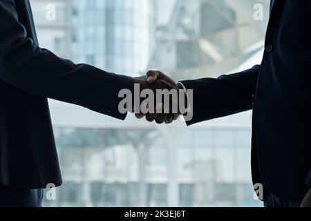 Handschlag von zwei jungen afroamerikanischen Geschäftsleuten in formalwear, die vor der Kamera stehen und einander gratulieren Stockfoto