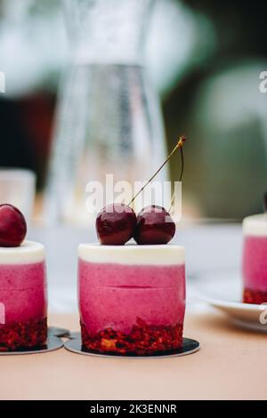 Köstlicher Plätzchen-Cupcake mit Schokoladenbasis und purpurfarbenem Zuckerguss, gekrönt mit einer blutroten Kirsche. Stockfoto