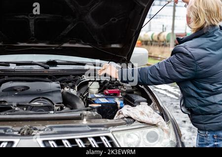 Ein Mann überprüft den Ölstand in einem Automotor mit einem Eisenmessstab. Technische Prüfung des Fahrzeugs. Stockfoto