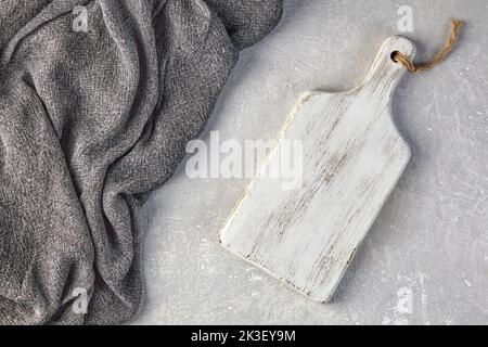 Weißer Holzschneideraum und graues Küchentuch auf einem hellgrauen Betontisch Stockfoto