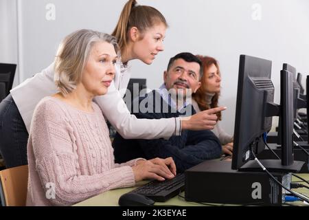 Seriöse Geschäftsfrau, die dem Mann hilft und auf den Computermonitor zeigt Stockfoto