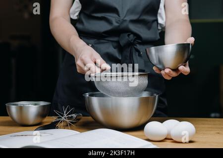 Junge weibliche Hände halten einen Teller mit Mehl über ein Sieb Nahaufnahme. Stockfoto