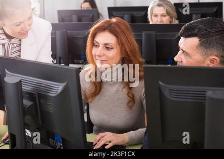 Junge Lehrerin hilft reifen Menschen, Computer zu benutzen Stockfoto