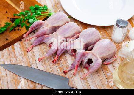 Rohe Wachteln mit Gemüse und Gewürzen, die zum Kochen auf einem Holztisch zubereitet werden Stockfoto