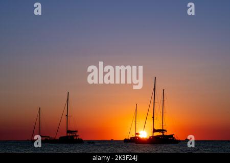 Drei Segelboote, die durch den Sonnenuntergang im Mittelmeer geschilhoutet wurden