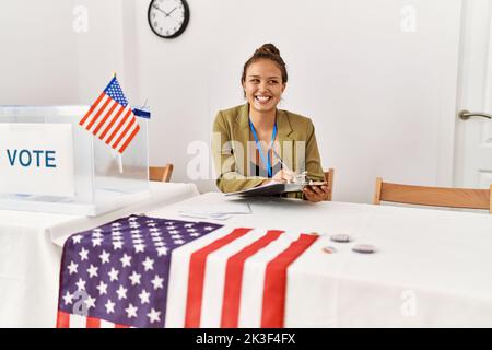 Junge schöne hispanische Frau Wahltisch Präsident schriftlich auf Zwischenablage an Wahlhochschule Stockfoto