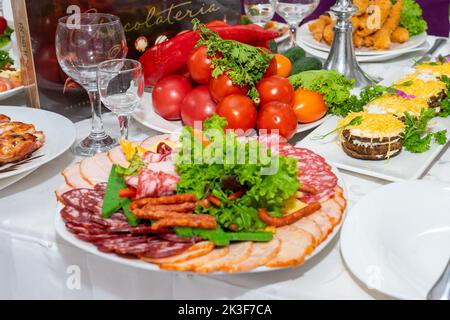 Ein Teller mit kalten Vorspeisen mit verschiedenen Würstchen, Fleisch und Käse. Grünpflanzen und Tomaten Stockfoto