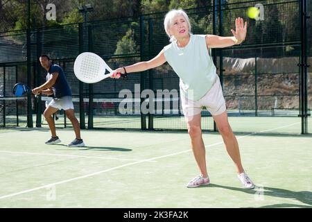 Sportliche ältere Frau, die im Sommer auf dem offenen Platz Padel spielt Stockfoto