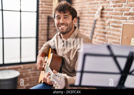 Junger Musiker, der im Musikstudio lächelnd und selbstbewusst klassische Gitarre spielt Stockfoto
