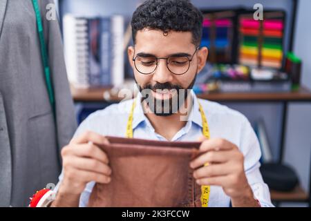 Junger arabischer Mann, Schneider, lächelnd, hält selbstbewusst Jeans in der Schneiderei Stockfoto