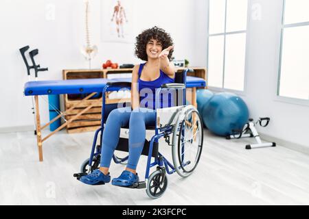 Junge Frau aus dem Nahen Osten, die auf dem Rollstuhl in der Physiotherapie-Klinik sitzt, lächelt freundlich und bietet Handschlag als Begrüßung und Begrüßung. Erfolgreicher Bus Stockfoto