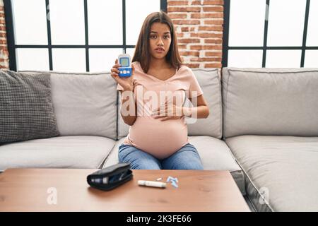 Junge Schwangere überprüfen Blutzucker ahnungslos und verwirrt Ausdruck. Zweifel Konzept. Stockfoto