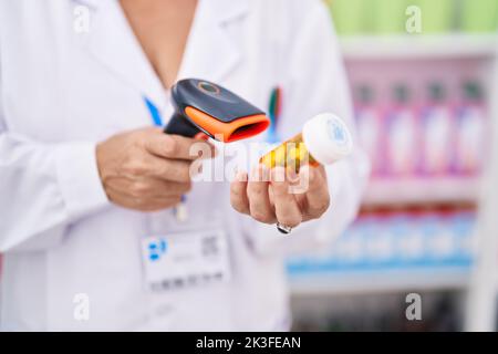Grauhaarige Frau im mittleren Alter, Apothekerin, die in der Apotheke eine Tablettenflasche scannt Stockfoto