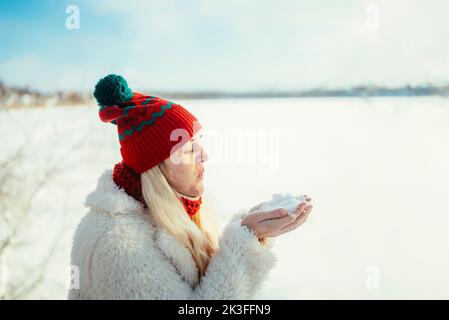 Portrait eines Mädchens in einem roten Hut und Schal, das an einem kalten Tag in einem verschneiten Wald auf dem Schnee weht. Stockfoto