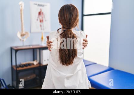 Junge Brünette Frau arbeitet in der Schmerzlinik umarmt sich glücklich und positiv von hinten. Selbstliebe und Selbstversorgung Stockfoto