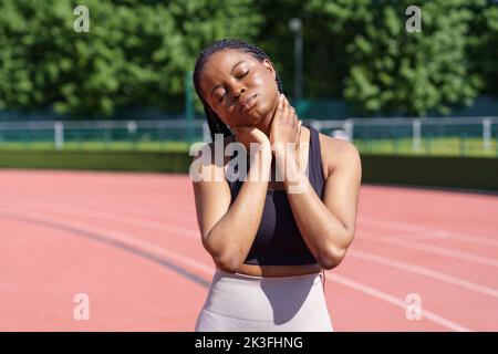 Afroamerikanische Frau streckt Körper und Hals und bereitet sich auf das Laufen auf der Strecke am sonnigen Morgen vor Stockfoto