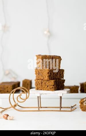 Weihnachts-Lebkuchenbäckerei auf dem Weihnachtsmannschlitten. Vegane Weihnachtskuchen mit Schokolade auf dem weißen Holztisch. Leuchtet im Hintergrund. Stockfoto