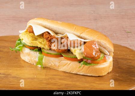 Frische U-Boot-Sandwiches mit Schinken, Käse, Speck, Tomaten, Salat, Gurken und Zwiebeln auf dunklem Holzhintergrund Stockfoto