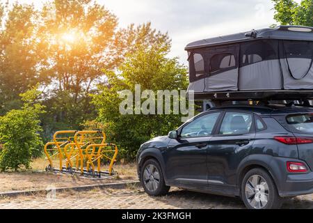 Modernes Wohnmobil-Wohnmobil mit Geländewagen und Dachzelt-Bett auf dem Parkplatz in der Nähe von Park oder Waldgebiet. Wohnmobil-Campingplatz Stockfoto