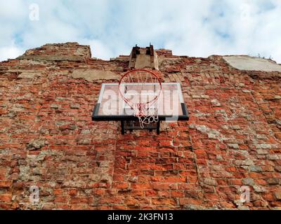 Altes und abgenutztes Outdoor-Basketballnetz auf dem Hintergrund der roten Backsteinmauer, urbaner Spielplatz, Innenstadt in der Stadt Stockfoto