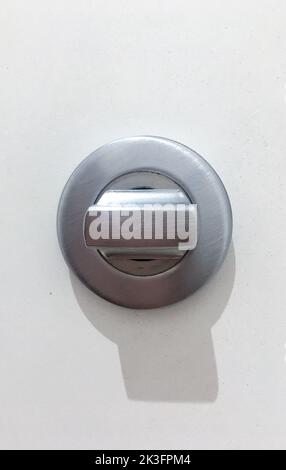 Abstrakte, hochpräzise Nahaufnahme mit einem glänzenden Metallgeländer und einer runden, schwarzen Befestigung an einer weißen Wand. Stockfoto