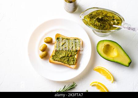 Toast mit Avocado, Oliven und Chimichurri-Sauce auf einem weißen Teller. Gesundes vegetarisches Essen. Weißer Hintergrund. Stockfoto