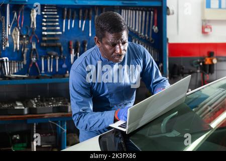 Afrikanischer Mechaniker, der in der Werkstatt ein Auto mit einem Laptop überprüft Stockfoto