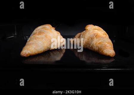 Zwei gebackene hausgemachte Croissants auf dem Tablett im elektrischen Ofen zu Hause Stockfoto