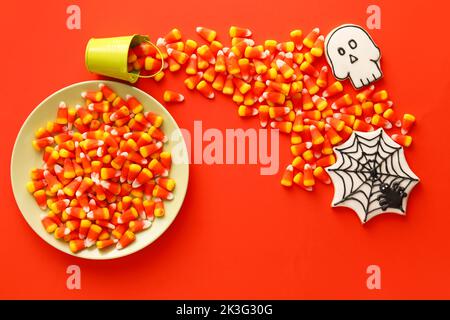 Teller, Eimer mit Halloween Bonbons und Keksen auf rotem Hintergrund Stockfoto