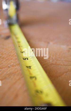 Nahaufnahme eines erweiterten Maßbands auf Sperrholzboden im Haus. Stockfoto