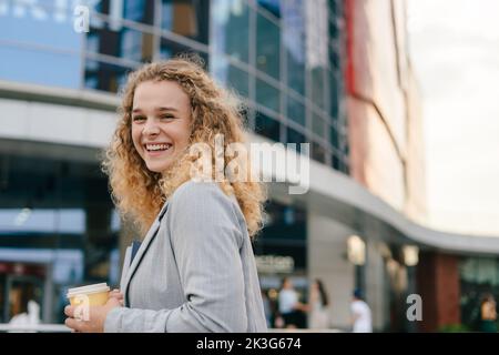 Junge attraktive glückliche Studentin, die einen Laptop mit einem Takeaway-Becher trägt. Schönheitsporträt. Sommer in der Natur. Kaffee trinken während der Pause Stockfoto