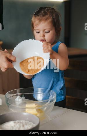 Die Mutter hilft ihrer Tochter, die Schüssel mit Kakao über den Teig zu drehen, der zum Backen zubereitet wird. Für Lifestyle-Design. Menschen leben. Stockfoto