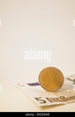 Nahaufnahme einer 5-Euro-Banknote und einer 2-Euro-Münze auf weißem Hintergrund. Stockfoto