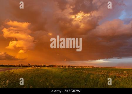 Ein schönes und gefährliches Gewitter zieht bei Sonnenuntergang über eine kleine Stadt und zeigt die orangen Gewitter, die sich in der Gegend bilden. Stockfoto