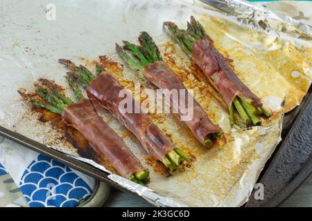 Gebackene Spargelbündel in Prosciutto-Scheiben auf Backblech mit Aluminiumfolie auf heißen Pads verpackt Stockfoto