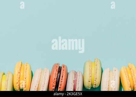 Französisches Dessertkonzept, Arrangement in einer Reihe von bunten Pastellmakronen auf hellblauem Hintergrund. Stockfoto
