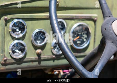 Gesprungenes Lenkrad des Fahrzeugs. Verschwommenes Armaturenbrett mit mechanischen Zifferblättern. Nahaufnahme. Selektiver Fokus auf schäbiges Lenkrad Stockfoto
