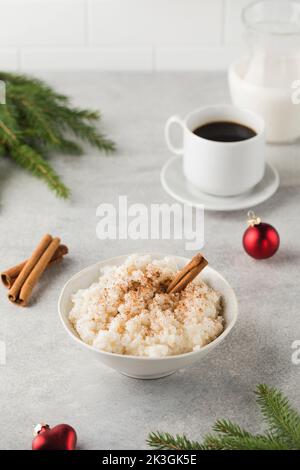 Skandinavischer Reisbrei mit Zimt in einer Schüssel, umgeben von Weihnachtskugeln. Frühstück am Heiligabend. Stockfoto