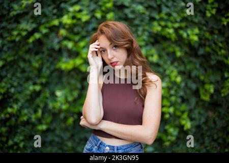 Porträt einer Frau mit besorgtem Ausdruck in einem Garten mit einer Kletterpflanze im Hintergrund Stockfoto