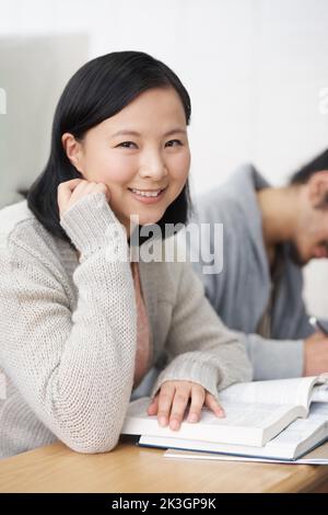 Wissen ist Macht. Eine asiatische Studentin lächelt der Kamera zu, während sie in der Klasse sitzt. Stockfoto