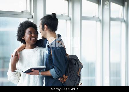 Beste Freunde. Ein studentisches Paar, das in den Universitätshallen steht und zusammen ein Lehrbuch anschaut. Stockfoto