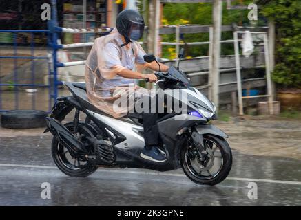 Ein Mann im Regenmantel fährt bei starkem Regen mit dem Motorrad auf die Straße Stockfoto