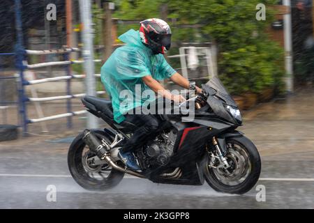 Ein Mann im Regenmantel fährt bei starkem Regen mit dem Motorrad auf die Straße Stockfoto