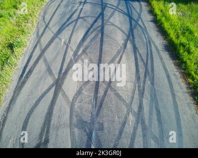 Reifenspuren auf der Luftaufnahme der Straße, die Muster von Gleitspuren und grünes Gras am Straßenrand, Victoria, Australien, zeigen. Stockfoto