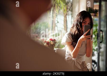 Lächelnde, verliebte junge Frau fotografiert heimlich ihren Schwarm im Coffeeshop Stockfoto