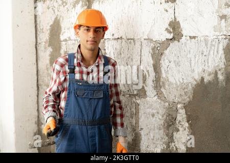 Muslimischer Baumeister mit Kelle und Zementmörtel auf weißem Backsteinwand-Hintergrund, Hausrenovierung und Umbaukonzept Stockfoto