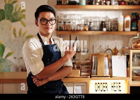 Porträt eines Barkeepers, der an der Theke steht und das Smartphone in den Händen hält Stockfoto