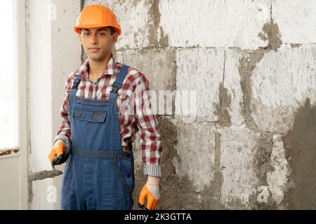 Arabischer Mann Meister putzt die Wände, Porträt des Baumeisters in Harthut macht Reparaturen in der Wohnung, das Konzept der Reparatur und Umbau der Hou Stockfoto