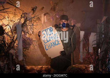 Umweltschutz. Ein Mann in einer Gasmaske hält ein Poster mit dem Wort STOP Climate change in Smoke. Umweltschutz. Luftverschmutzung. Schädlich Stockfoto