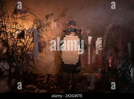 Mann in einer Gasmaske mit Plakaten mit Worten gibt es keinen Planeten B. Verbrennen von Plastikmüll und Rauch auf dem Hintergrund. Umweltprobleme: Kunststoff Stockfoto